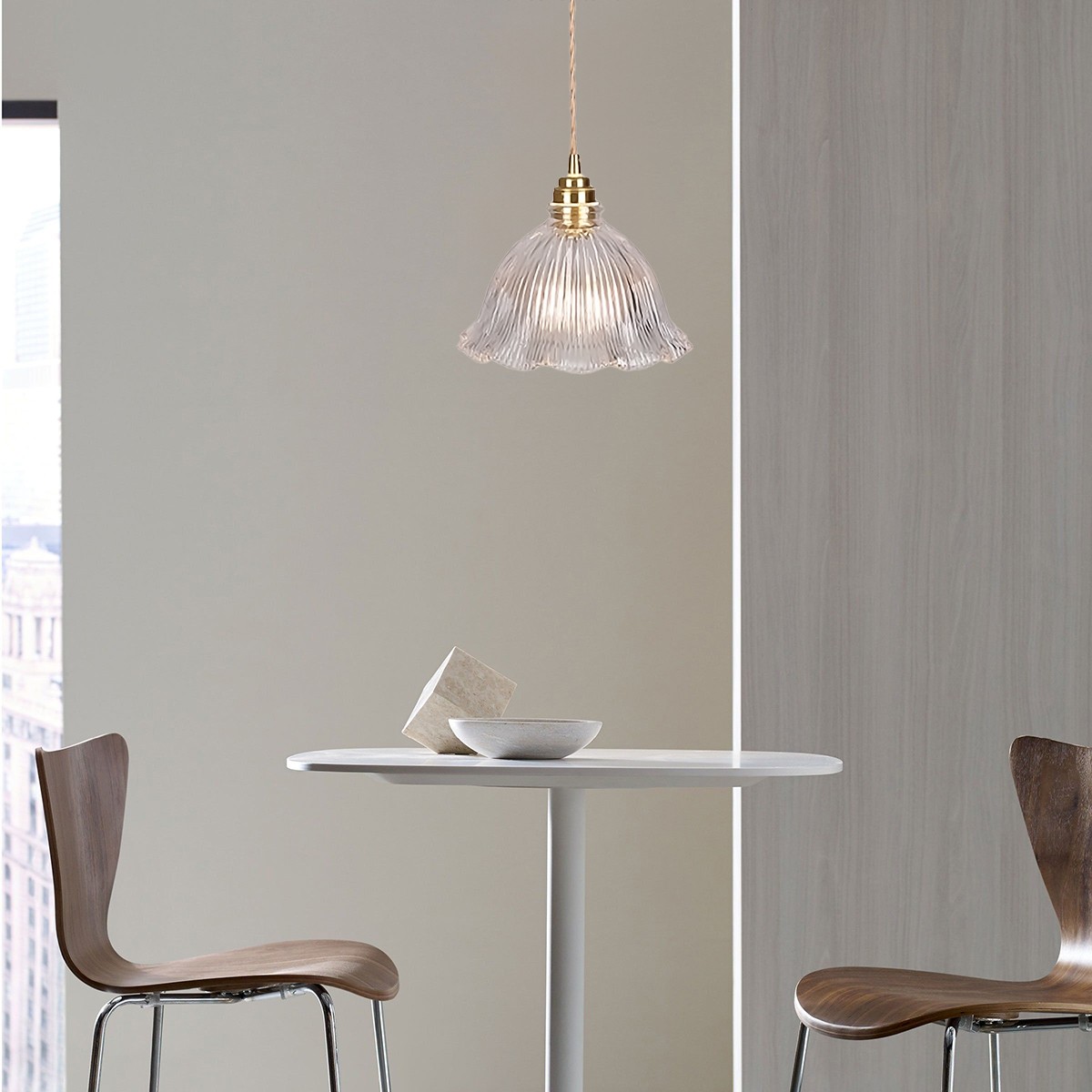 Vista a escala de la habitación de la lámpara colgante de cristal con forma de flor sobre una pequeña mesa de comedor.