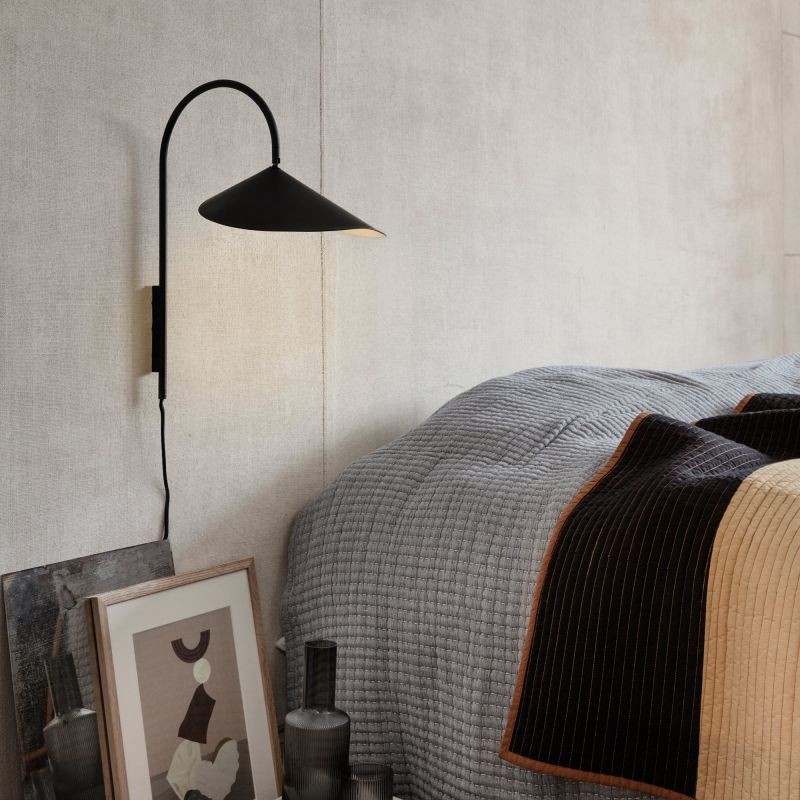 Black leaf-shaped wall lamp mounted near bed