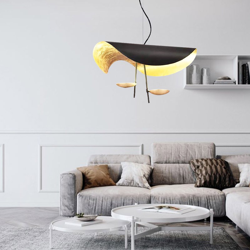 Schwarze und goldene Pendelleuchte mittig über den Sitzgelegenheiten im Wohnzimmer.