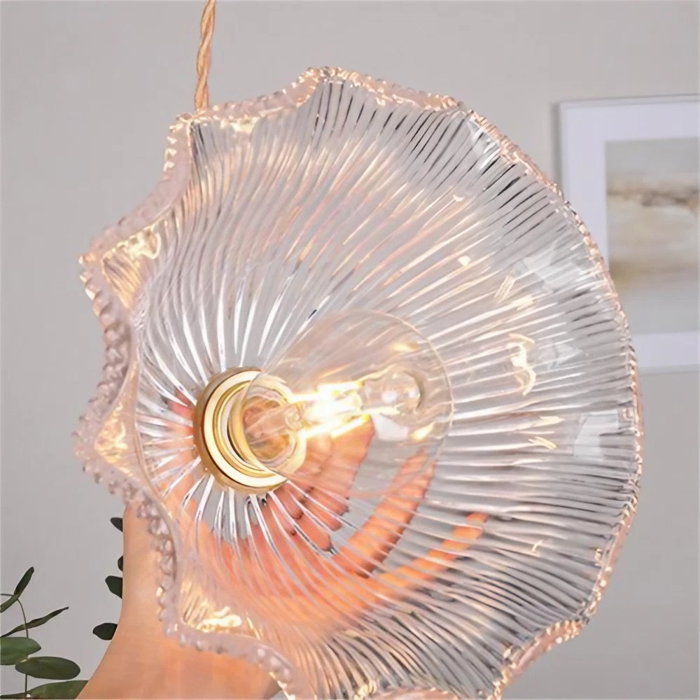 Detalle de la pantalla de cristal con forma de flor acanalada y el cálido resplandor de la bombilla.