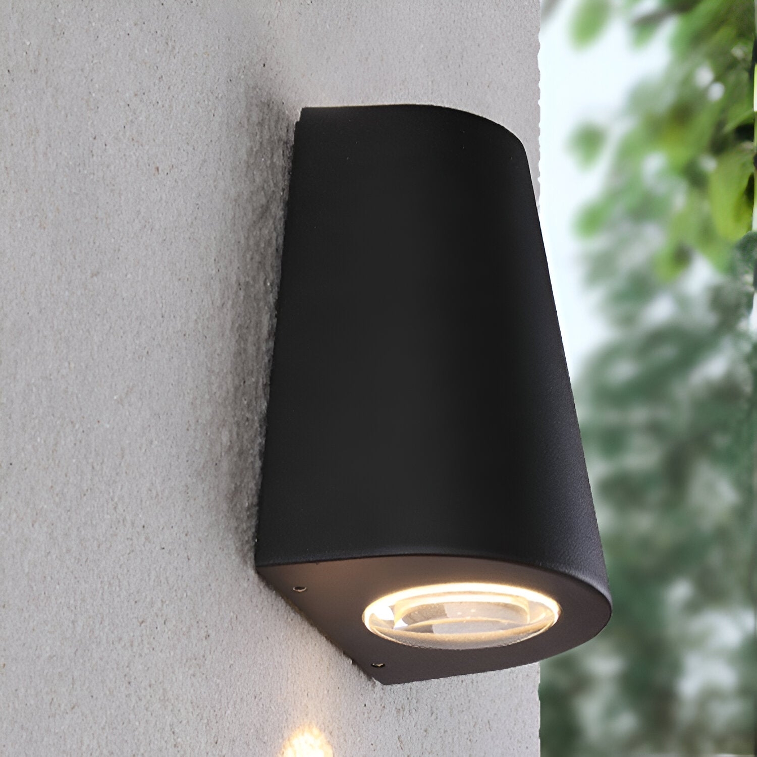 Aplique de pared exterior negro de instalación cercana con luz cálida y fondo de follaje.