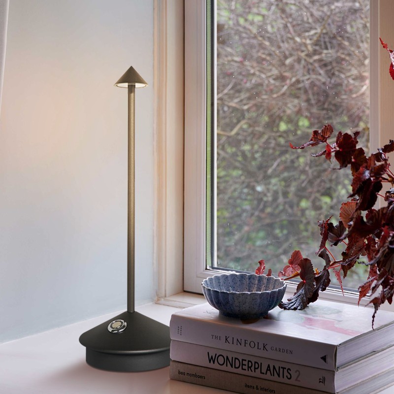 Lampa Pina na książkach przy oknie z roślinami
