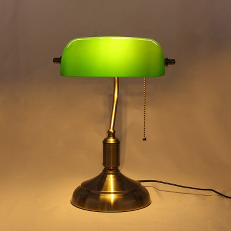 Green banker lamp lit against a warm background