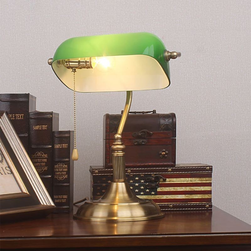 Green banker lamp in desk vignette with books and decorative boxes