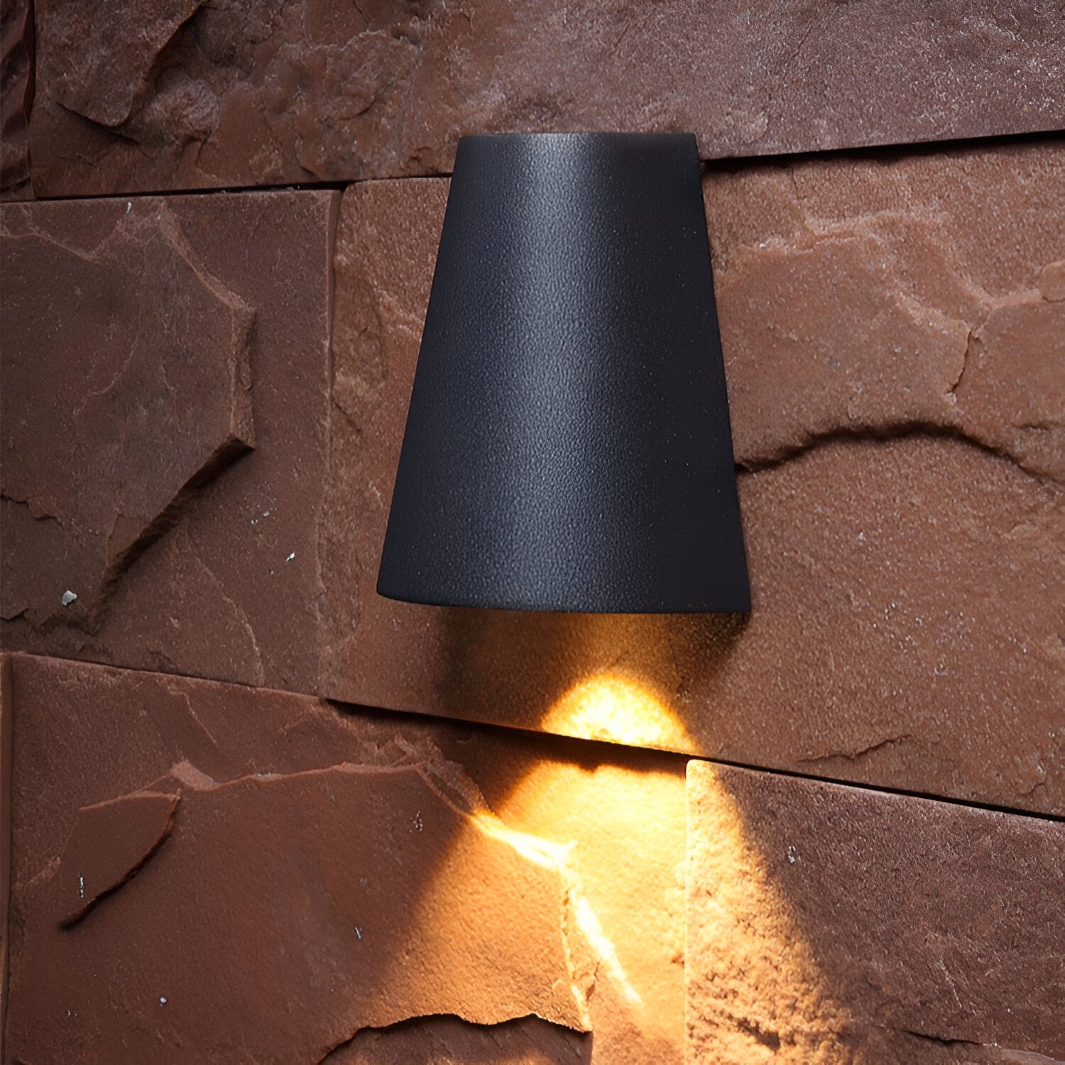 Vista de cerca de una luz negra iluminada en una pared de piedra texturizada, que refleja un estilo de vida cotidiano.