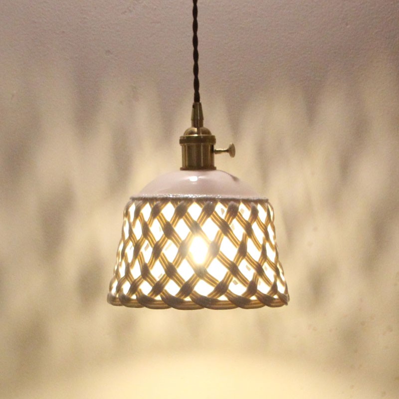 Lampada a sospensione in ceramica traforata illuminata da una luce diffusa che crea un motivo a parete.