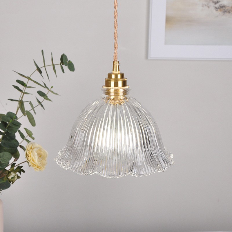 Lámpara colgante de cristal transparente en un interior con plantas y decoración de pared.