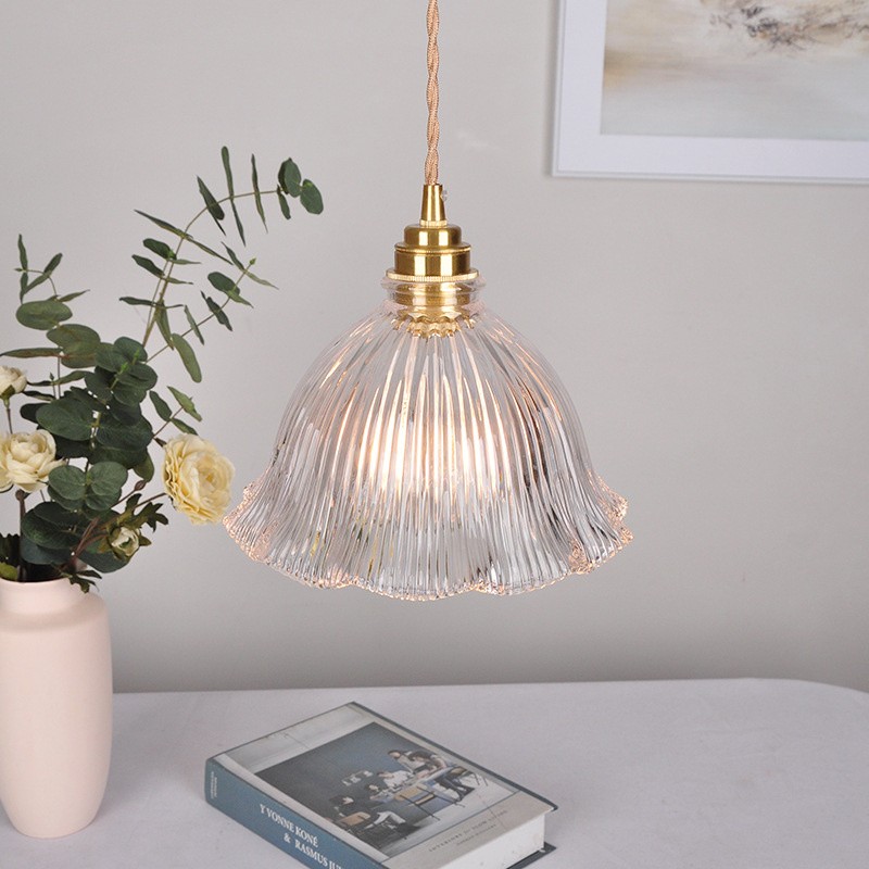 Lámpara colgante transparente ilumina una mesa con objetos decorativos.