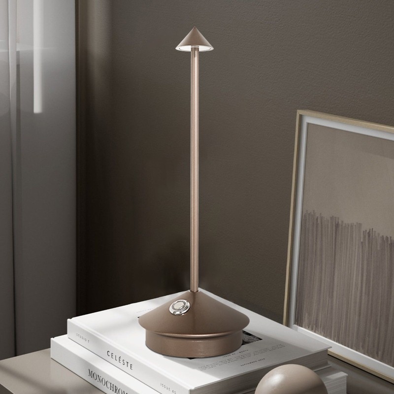 Lampa Pina na ułożonych książkach obok oprawionej grafiki