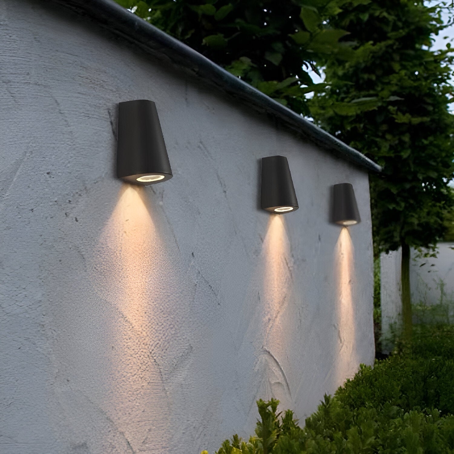 Muro del jardín con tres luminarias exteriores de luz cálida instaladas en fila.