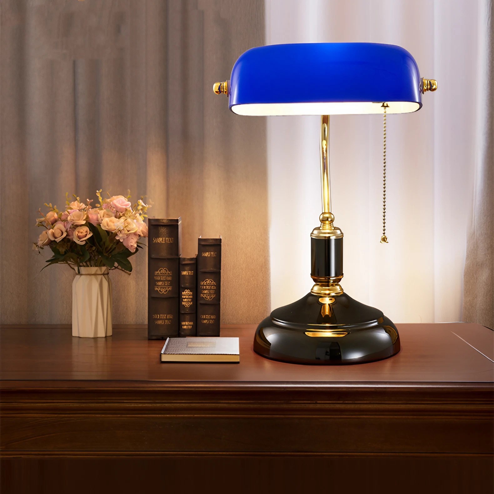 Blue banker lamp on desk with books and flowers