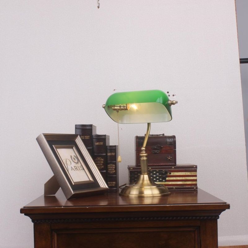 Green banker lamp on a desk with books and frame