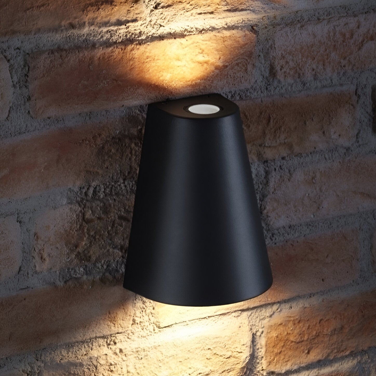 Aplique de pared exterior con iluminación hacia arriba y hacia abajo, montado sobre una pared de ladrillo.