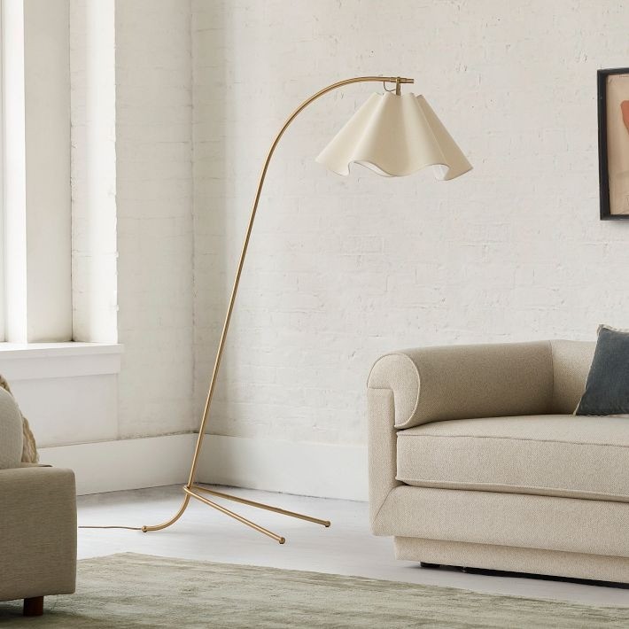 Guldfärgad välvd golvlampa Oslan bredvid en soffa i ett vardagsrum